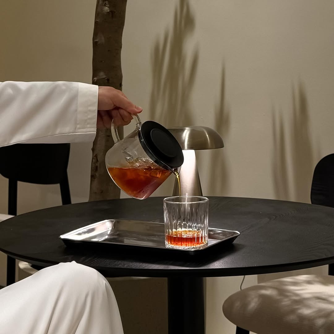 Tea being poured into a glass on a dark table